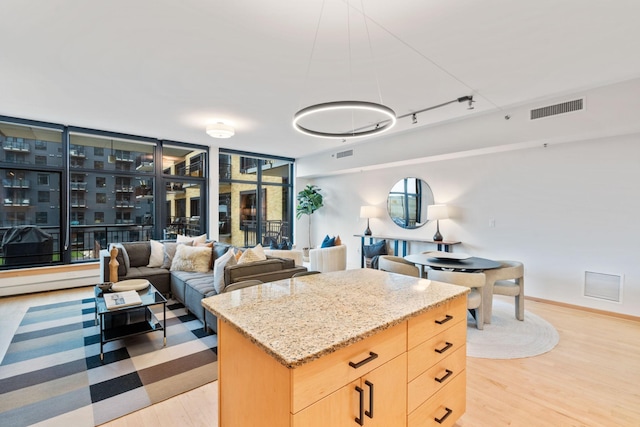 kitchen featuring light brown cabinetry, light wood-type flooring, track lighting, light stone counters, and a kitchen island