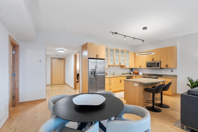 kitchen featuring light brown cabinetry, appliances with stainless steel finishes, pendant lighting, a center island, and light hardwood / wood-style floors