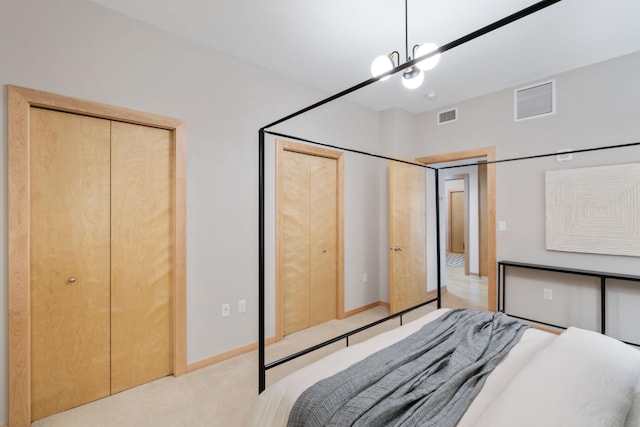 bedroom featuring a chandelier, light carpet, and two closets