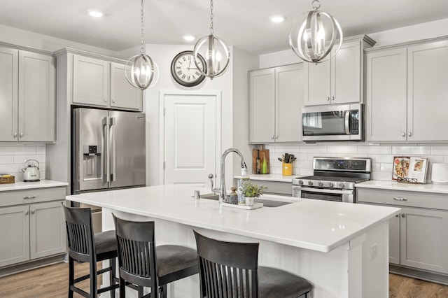 kitchen with sink, a kitchen island with sink, gray cabinetry, and appliances with stainless steel finishes