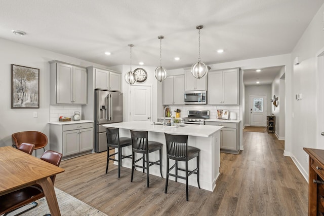 kitchen featuring decorative light fixtures, gray cabinets, an island with sink, and appliances with stainless steel finishes