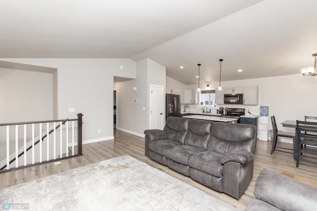 living room featuring sink, light hardwood / wood-style floors, lofted ceiling, and a notable chandelier