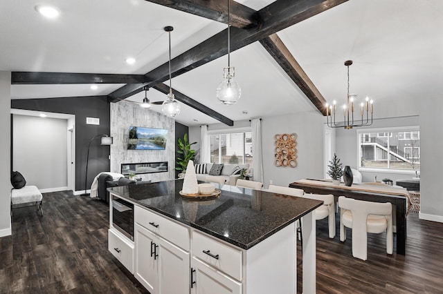 kitchen featuring built in microwave, white cabinetry, pendant lighting, dark stone counters, and a kitchen island