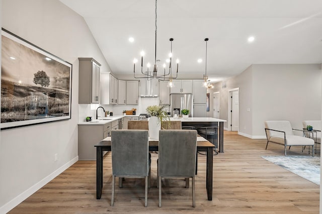 dining area with a chandelier, light wood-type flooring, sink, and vaulted ceiling