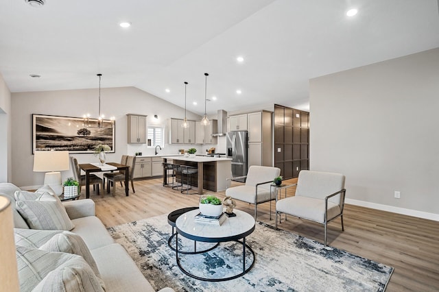 living room featuring an inviting chandelier, light hardwood / wood-style flooring, lofted ceiling, and sink