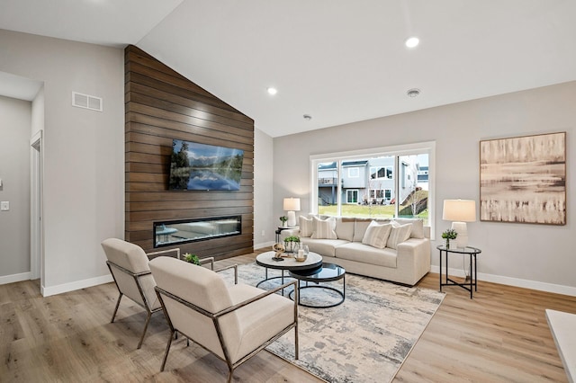 living room featuring a large fireplace, light hardwood / wood-style floors, and vaulted ceiling