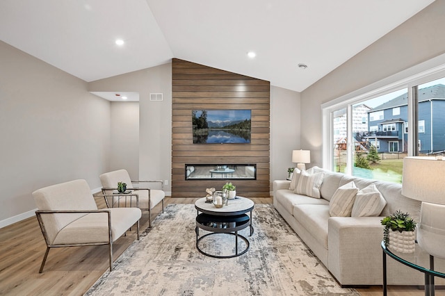 living room featuring a large fireplace, light wood-type flooring, and vaulted ceiling