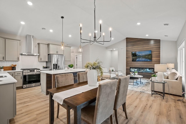 dining area with light wood-type flooring, a large fireplace, vaulted ceiling, and a notable chandelier