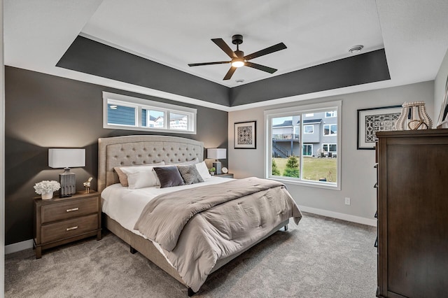 carpeted bedroom with multiple windows, a tray ceiling, and ceiling fan