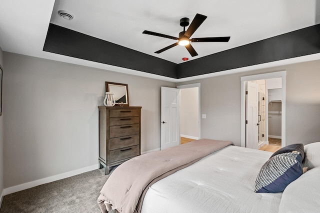 bedroom featuring light colored carpet, ceiling fan, a raised ceiling, and a walk in closet