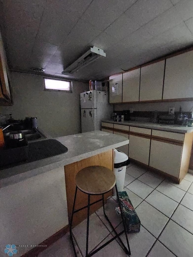 kitchen with white refrigerator, white cabinetry, a kitchen bar, and light tile patterned flooring