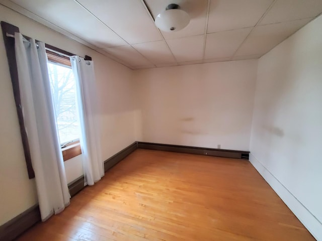 empty room featuring a baseboard radiator, light hardwood / wood-style flooring, and a drop ceiling