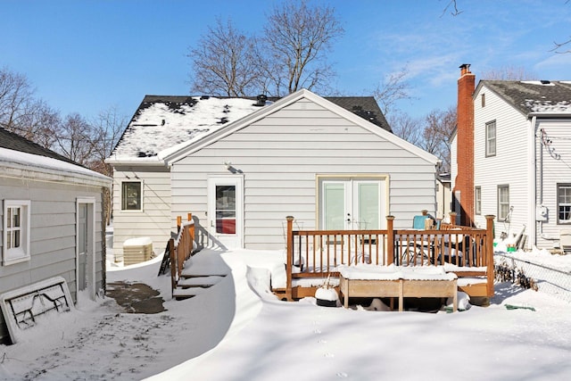 snow covered rear of property featuring french doors and a deck