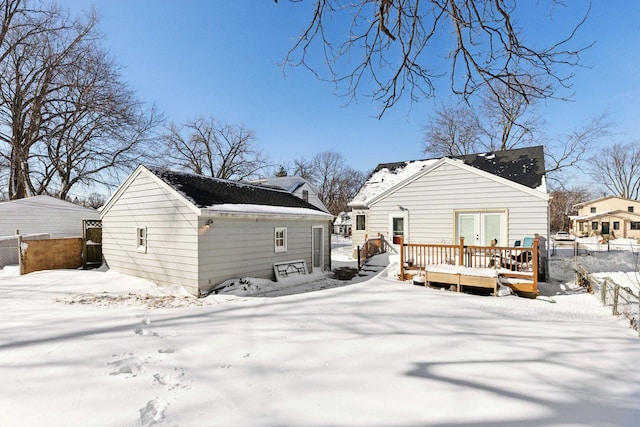 snow covered back of property featuring french doors, a wooden deck, an outdoor structure, and fence