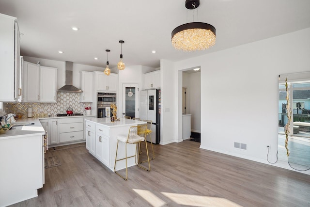 kitchen with wall chimney exhaust hood, decorative backsplash, a center island with sink, white cabinets, and appliances with stainless steel finishes