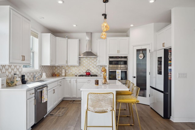 kitchen with white cabinetry, wall chimney exhaust hood, stainless steel appliances, and a kitchen island