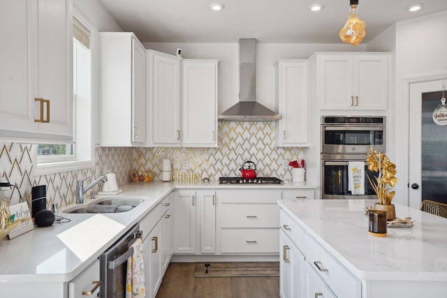 kitchen featuring wall chimney range hood, sink, decorative light fixtures, white cabinetry, and stainless steel appliances