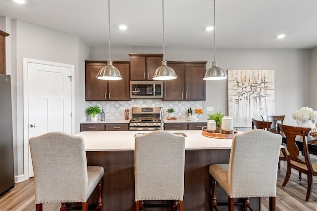 kitchen with tasteful backsplash, a breakfast bar, stainless steel appliances, hanging light fixtures, and an island with sink