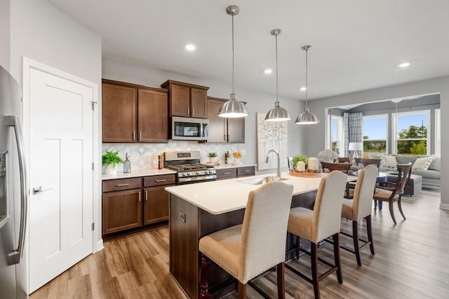 kitchen with appliances with stainless steel finishes, a breakfast bar, a kitchen island with sink, sink, and pendant lighting