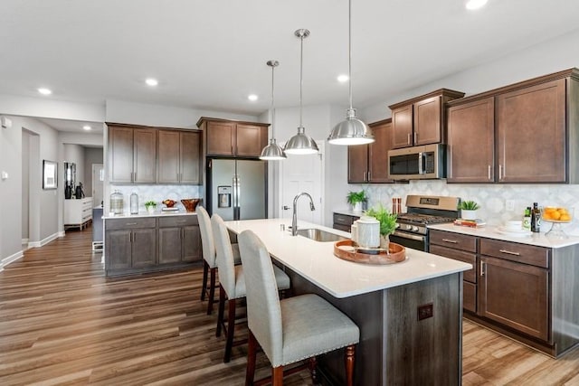 kitchen featuring sink, hanging light fixtures, stainless steel appliances, backsplash, and a center island with sink