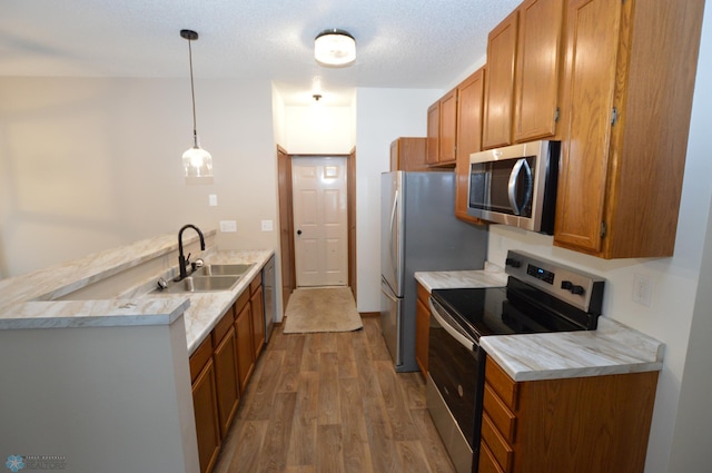 kitchen featuring appliances with stainless steel finishes, a textured ceiling, sink, wood-type flooring, and hanging light fixtures