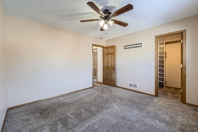 unfurnished bedroom featuring ceiling fan, a walk in closet, a closet, and carpet floors