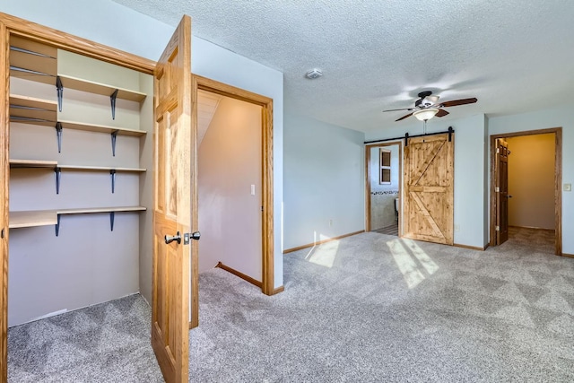 unfurnished bedroom with a textured ceiling, ceiling fan, carpet, and a barn door