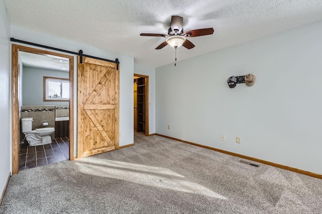 unfurnished bedroom with ensuite bathroom, dark carpet, a closet, a barn door, and a walk in closet