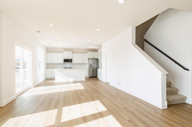 unfurnished living room with light wood-style floors, stairway, and recessed lighting