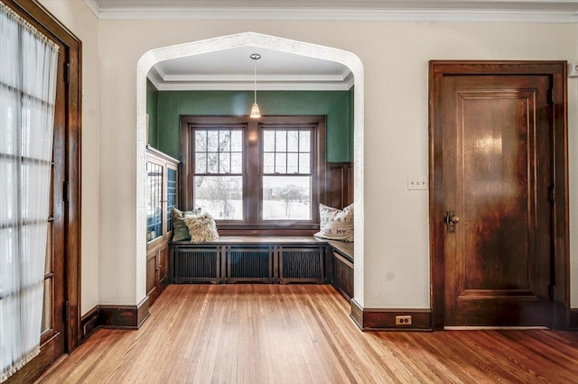 interior space featuring ornamental molding, light wood-type flooring, arched walkways, and baseboards