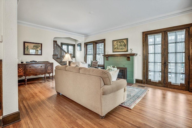 living room featuring arched walkways, ornamental molding, wood finished floors, a tile fireplace, and stairs