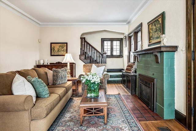 living room featuring arched walkways, a tiled fireplace, ornamental molding, wood finished floors, and stairs