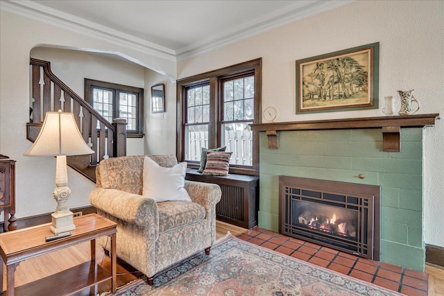 sitting room featuring arched walkways, a tiled fireplace, radiator, stairway, and ornamental molding