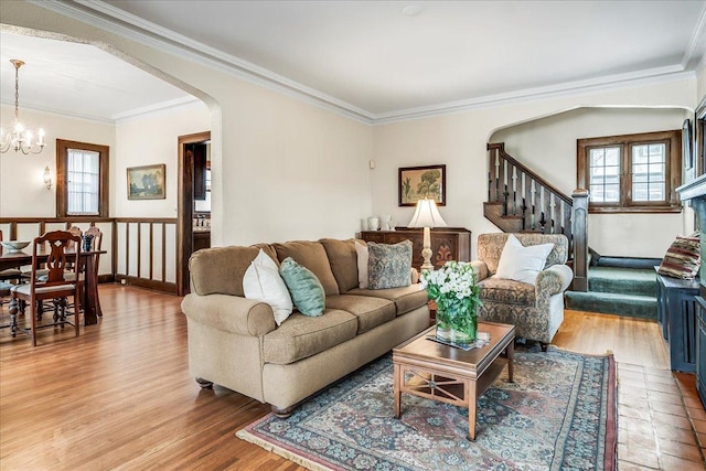 living room with arched walkways, light wood-style flooring, stairway, ornamental molding, and an inviting chandelier