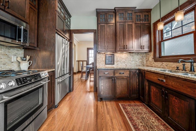 kitchen with stainless steel appliances, light wood-style flooring, decorative backsplash, a sink, and light stone countertops