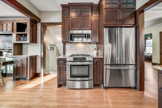 kitchen with appliances with stainless steel finishes, light wood-type flooring, dark brown cabinets, and decorative backsplash