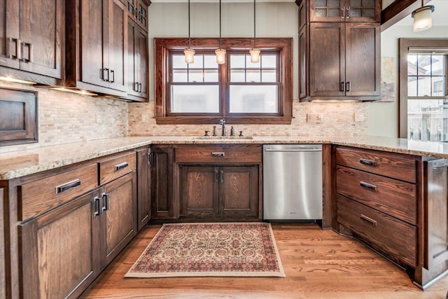 kitchen featuring light stone counters, light wood finished floors, decorative backsplash, a sink, and dishwasher