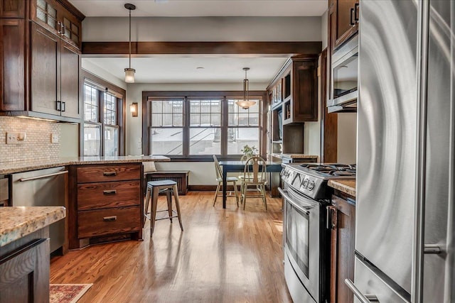 kitchen featuring decorative backsplash, glass insert cabinets, stainless steel appliances, light wood-style floors, and pendant lighting