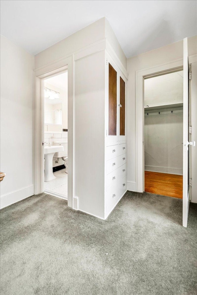 unfurnished bedroom with a spacious closet, carpet, ensuite bath, and baseboards