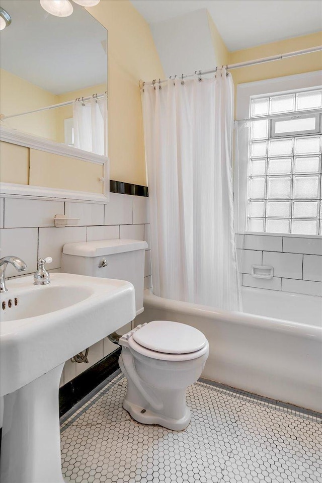 full bath with toilet, a wainscoted wall, shower / tub combo with curtain, tile patterned floors, and tile walls