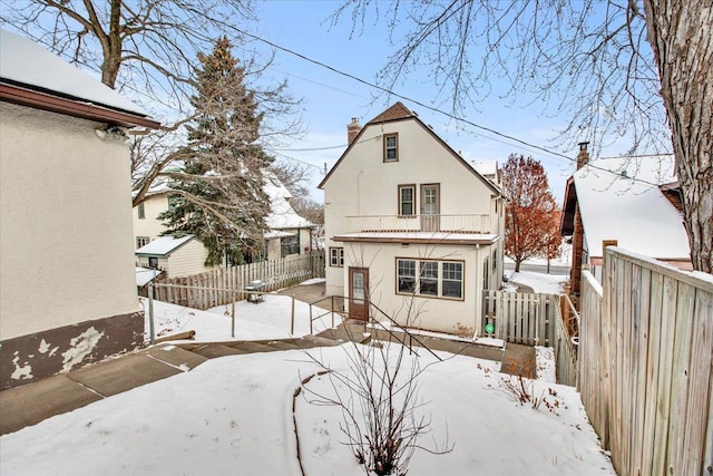 snow covered back of property with a balcony, a fenced backyard, and stucco siding