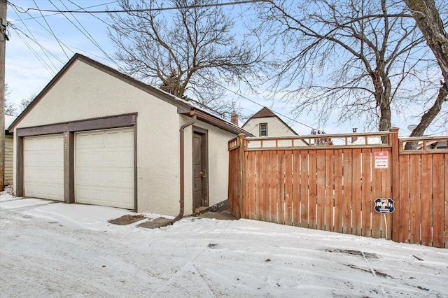 snow covered garage with fence and a detached garage