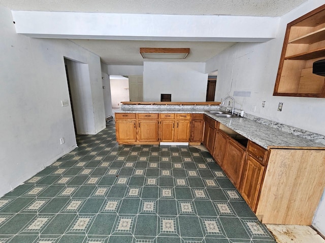 kitchen with beam ceiling, kitchen peninsula, sink, and a textured ceiling