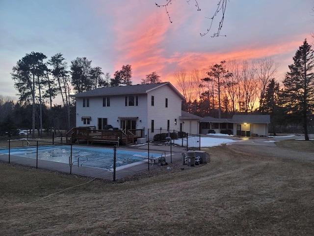 pool at dusk featuring a deck, a fenced in pool, and fence