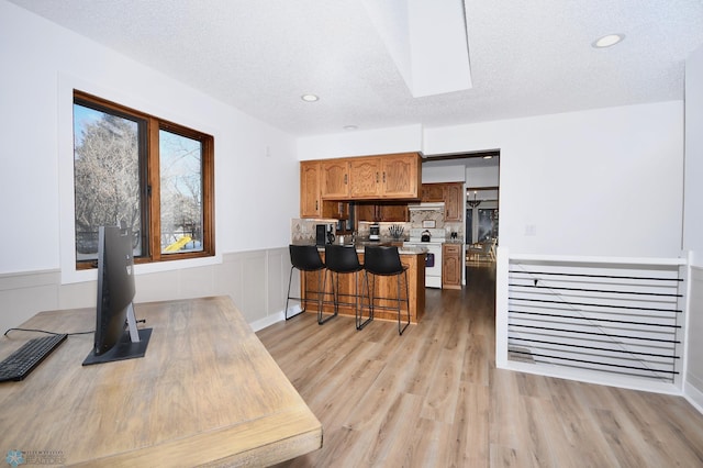 kitchen with a kitchen breakfast bar, white range, a textured ceiling, light hardwood / wood-style floors, and kitchen peninsula