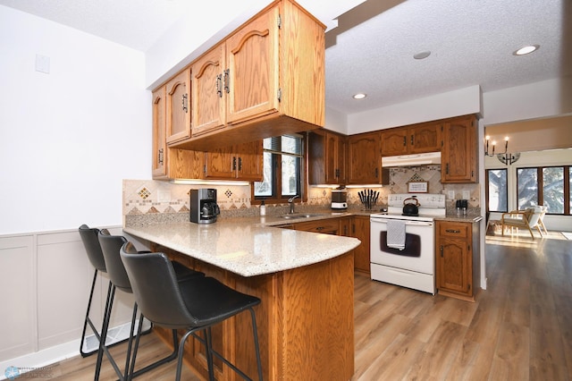 kitchen featuring kitchen peninsula, a kitchen breakfast bar, a chandelier, white electric range, and light hardwood / wood-style floors