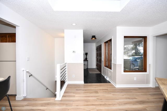 corridor with light wood-type flooring and a textured ceiling