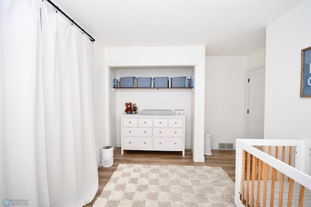 bedroom with a textured ceiling, wood-type flooring, and a crib