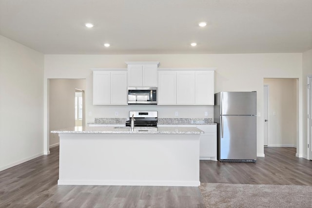 kitchen featuring white cabinets, a center island with sink, light stone countertops, wood-type flooring, and stainless steel appliances