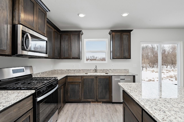 kitchen with dark brown cabinets, stainless steel appliances, light stone counters, and sink